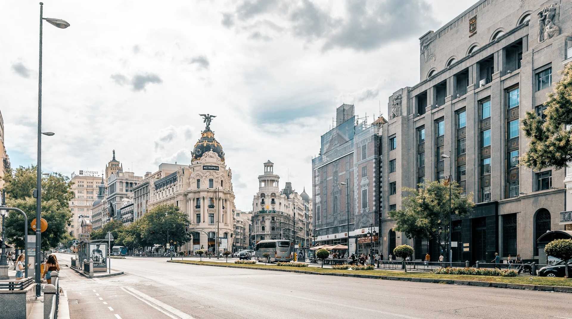 Calle Gran Vía en Madrid con edificios icónicos y cielo nublado.