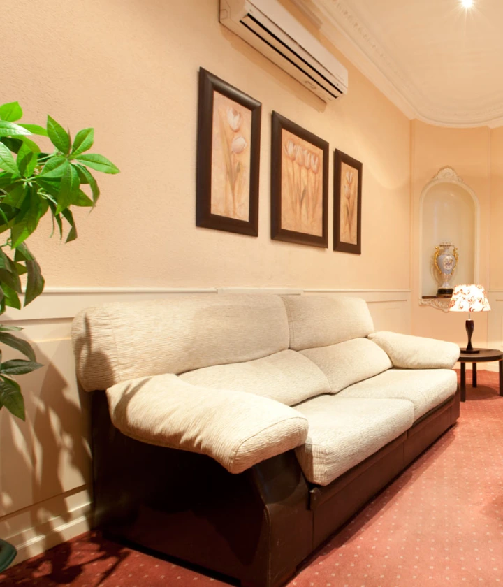 Sala acogedora con sofá beige, cuadros de flores y lámpara sobre mesa.