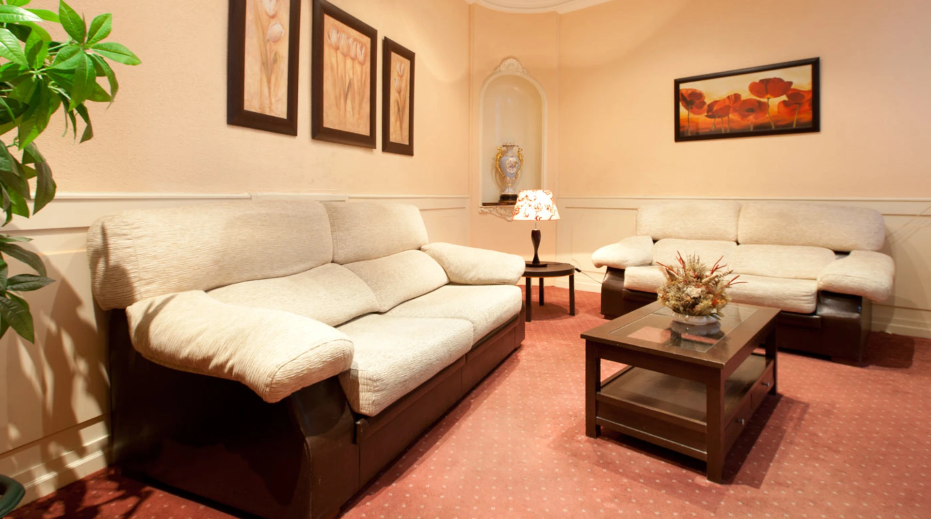 Sala acogedora con sofás beige, mesa de centro, cuadros florales y lámpara en alfombra roja.