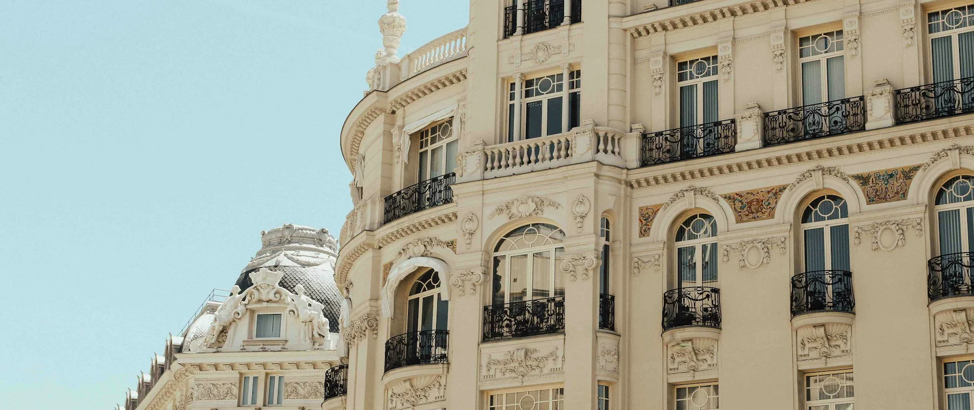 Edificio histórico con balcones de herrería y detalles decorativos sobre fondo de cielo azul.
