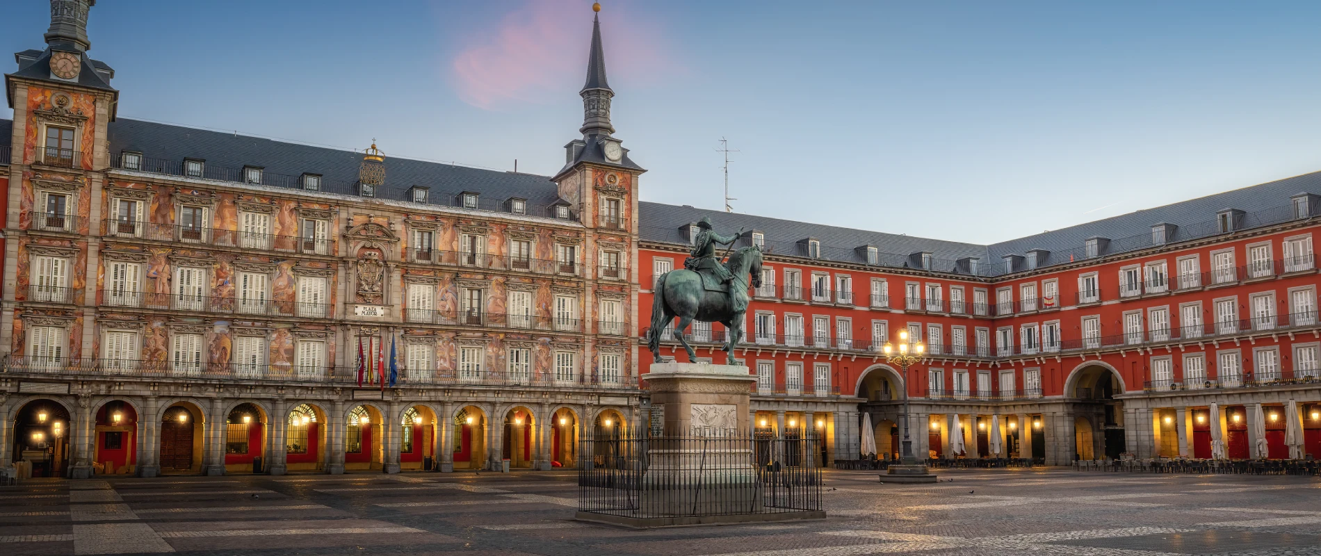 Plaza Mayor de Madrid al atardecer, con estatua ecuestre en el centro y edificios históricos alrededor.