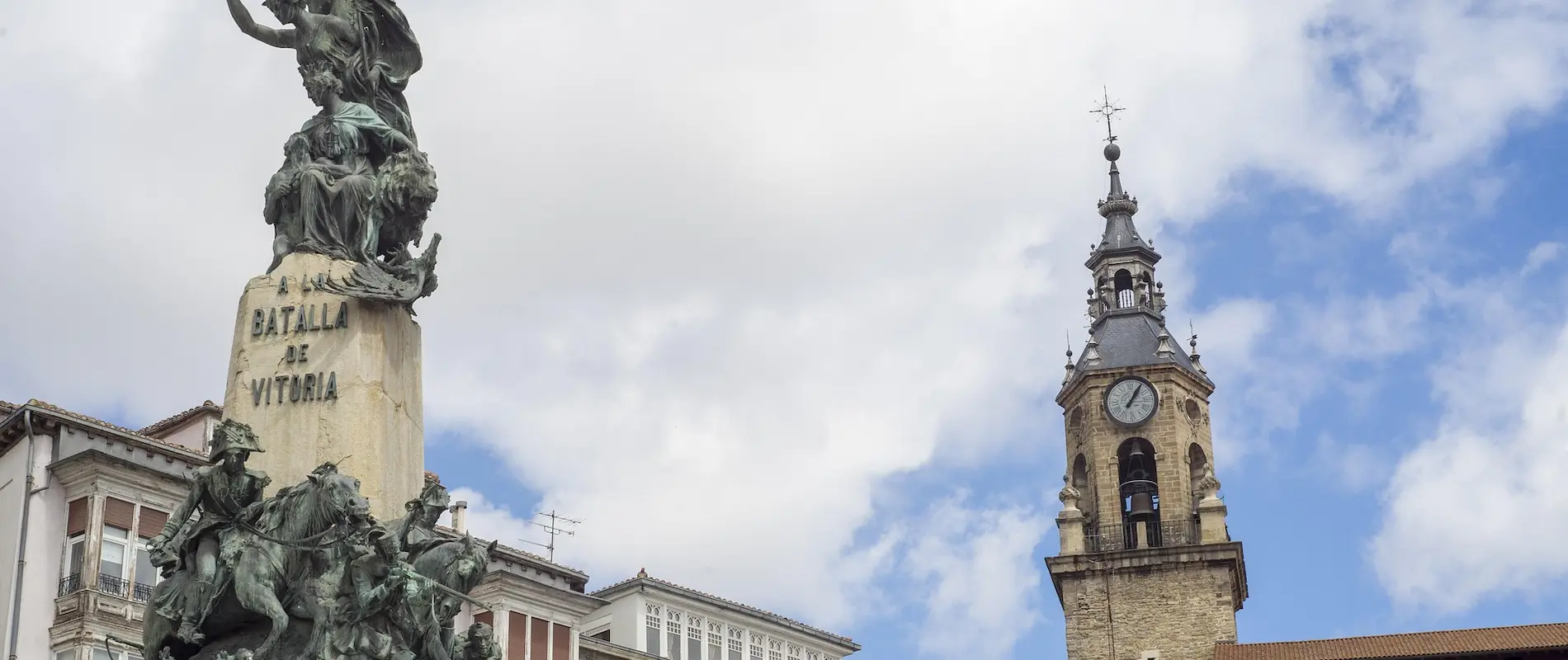 Monumento a la Batalla de Vitoria y torre del reloj bajo un cielo parcialmente nublado.
