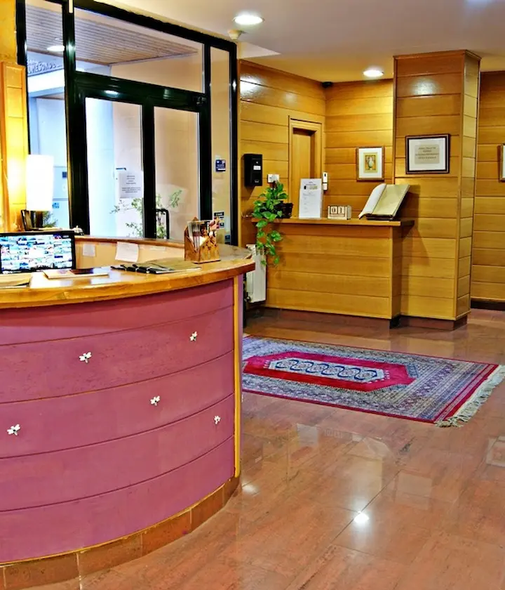 Recepción de hotel con mostrador curvo, alfombra roja y paredes revestidas de madera iluminadas.