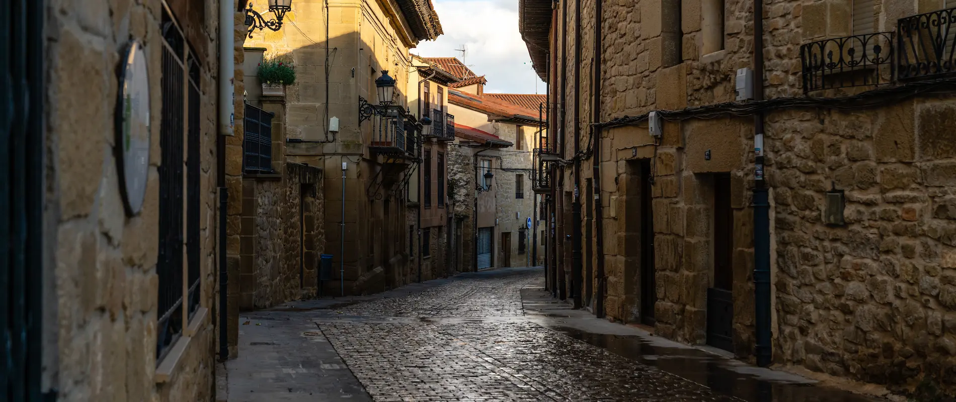 Calle estrecha con edificios de piedra y faroles antiguos al atardecer.