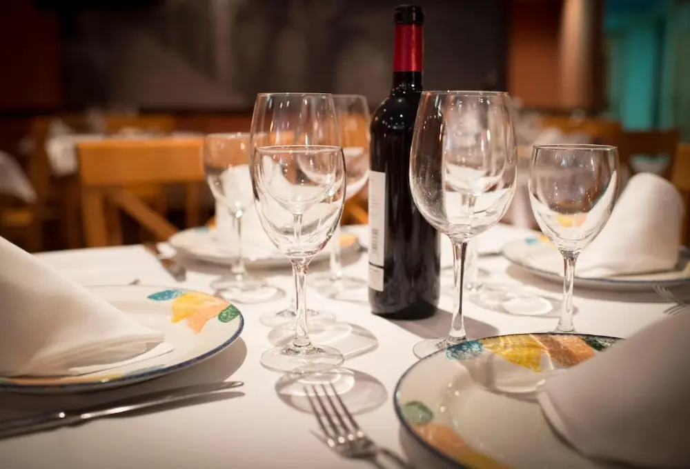 Mesa elegante con copas, platos decorados y botella de vino.