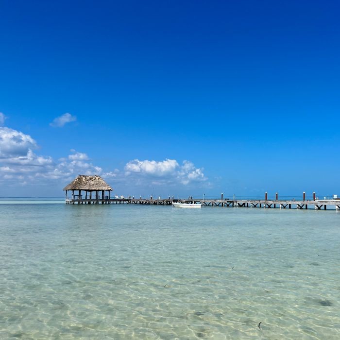 A pier with a thatched hut on clear water under a blue sky.