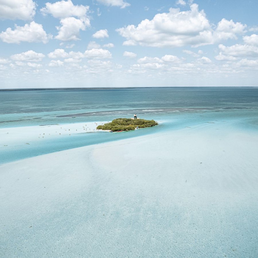 A small island surrounded by turquoise ocean under a blue sky with clouds.