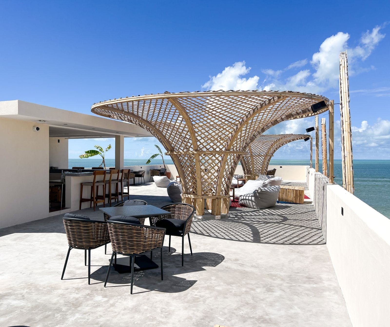 Beachside terrace with wicker seating under lattice canopies.