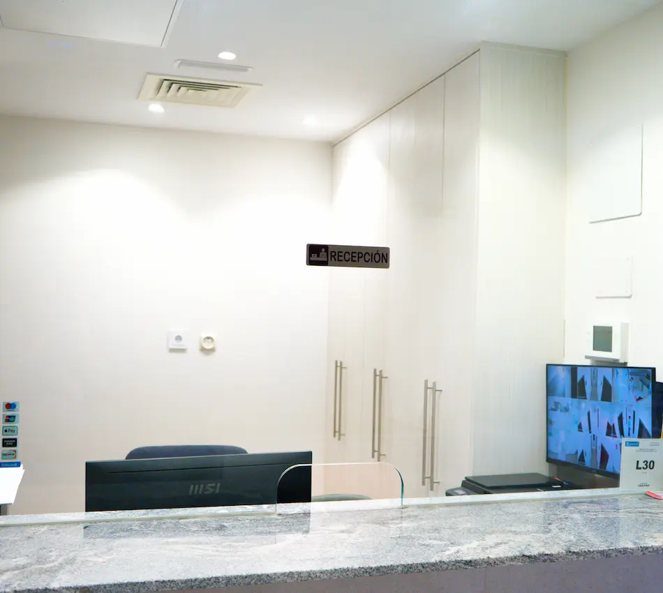 Mostrador de recepción con monitor y carteles en una oficina luminosa.