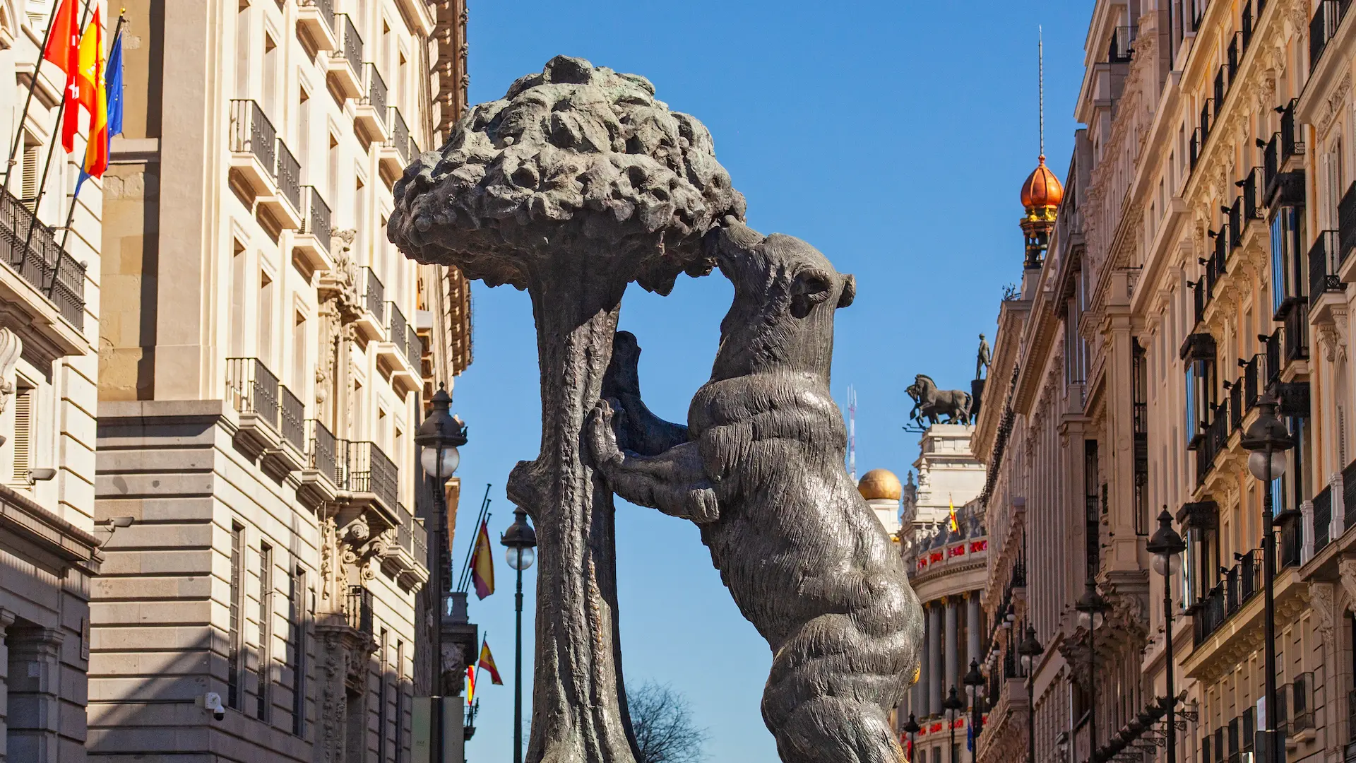 Estatua del oso y el madroño en una calle de Madrid, entre edificios.