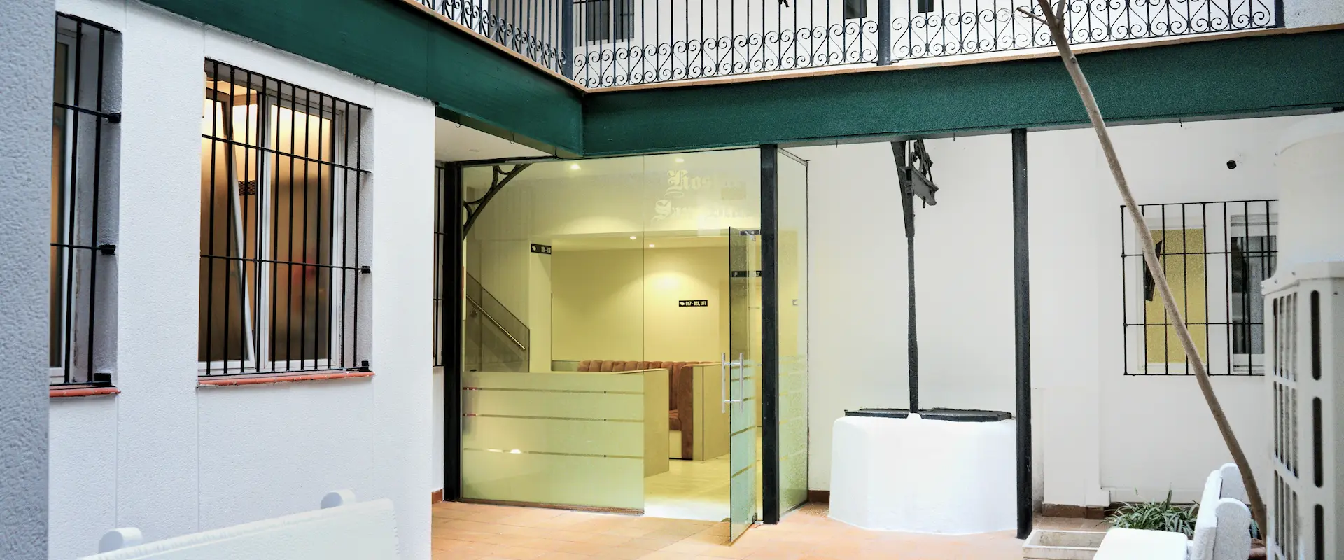 Patio interior con ventanas enrejadas, puerta de vidrio y barandilla de hierro en el techo.