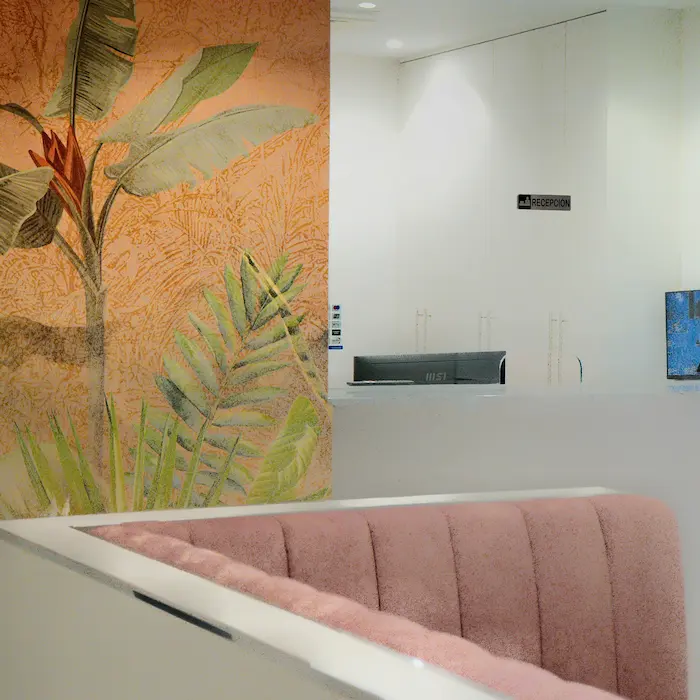 Recepción moderna con sofá rosa y mural de hojas tropicales en la pared iluminada.