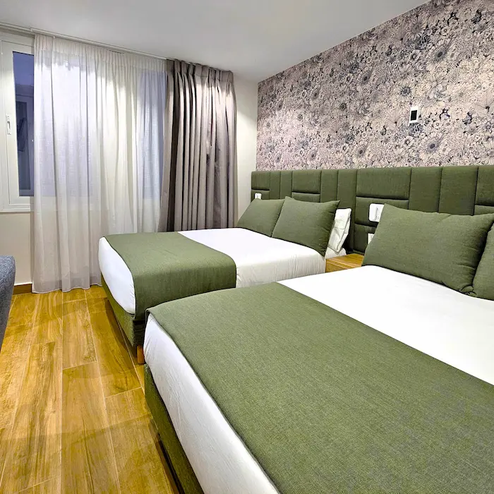 Habitación moderna con dos camas, ropa verde, paredes decoradas y cortinas largas.