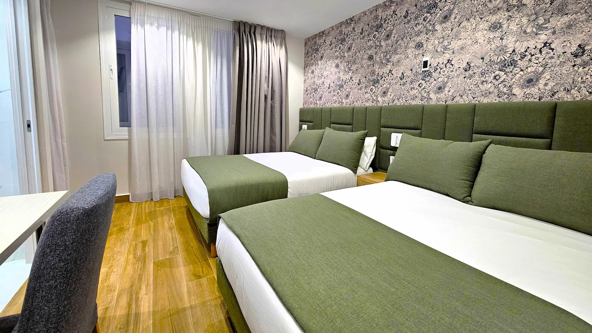 Habitación de hotel con dos camas, colchas verdes y pared decorativa floral.