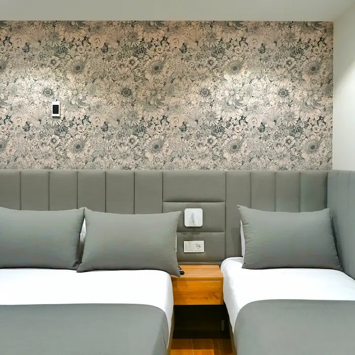 Habitación con dos camas, cabecera gris y papel tapiz floral en la pared del fondo.