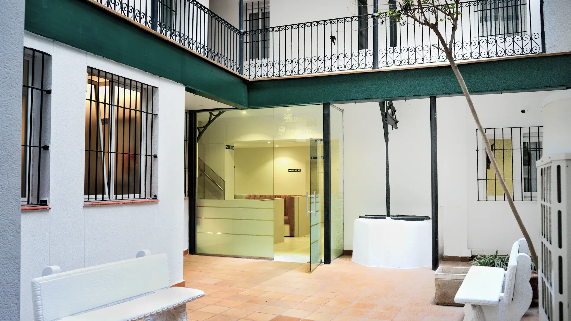 Patio interior con bancos, puertas de vidrio y barandas metálicas decorativas.