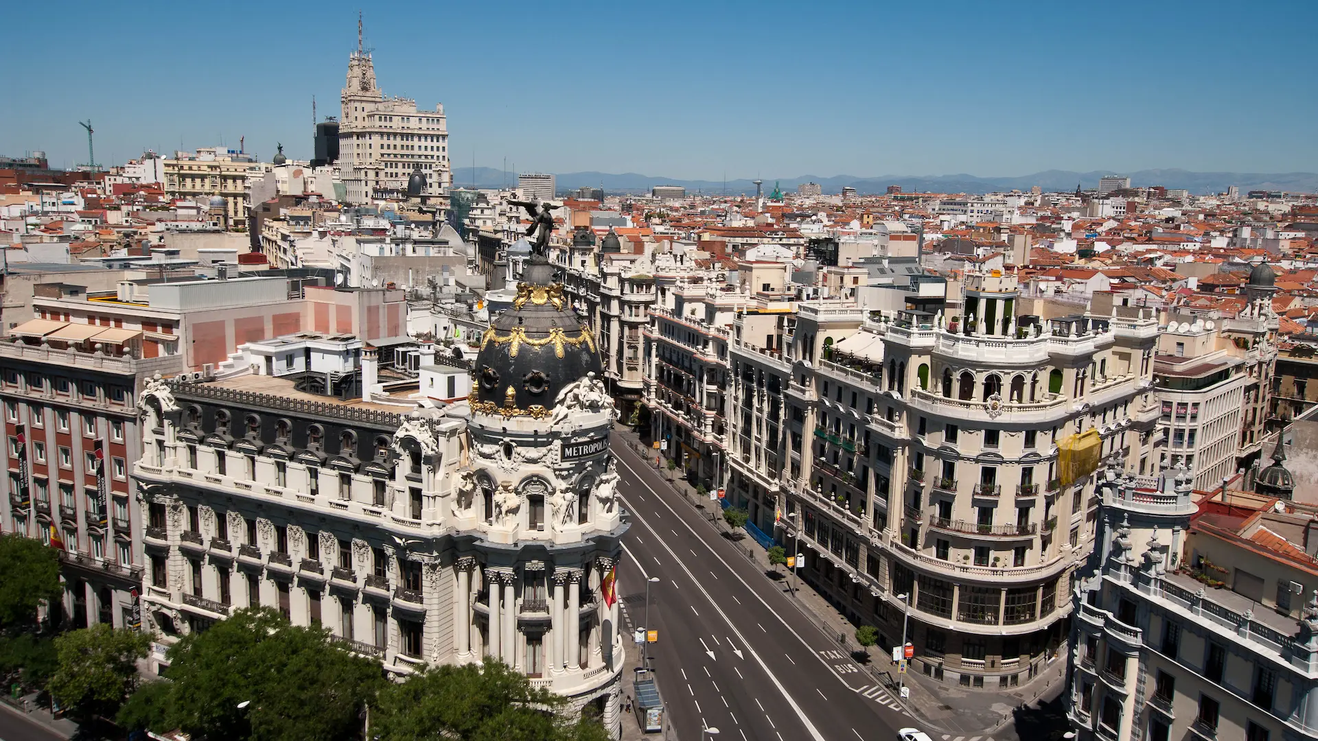 Vista aérea de un edificio histórico en una ciudad, con una calle amplia y cielo despejado.