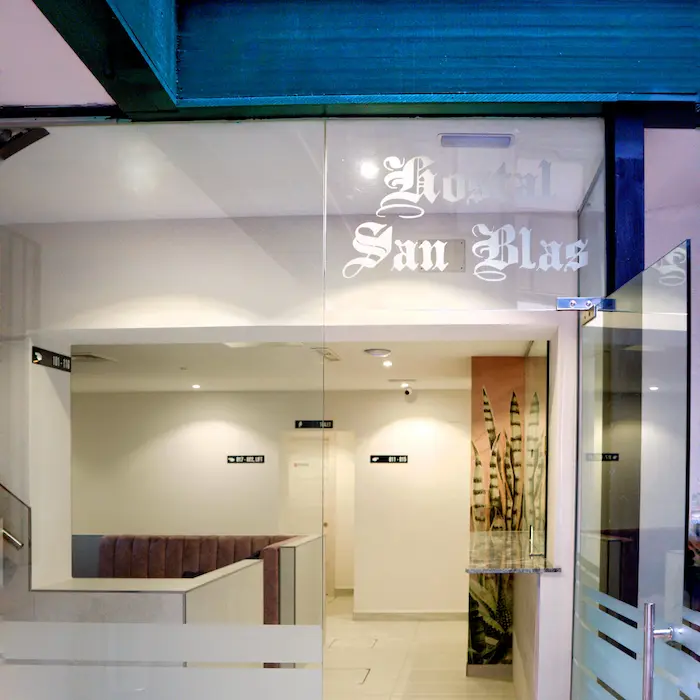Entrada del Hostal San Blas con puertas de vidrio y plantas decorativas.
