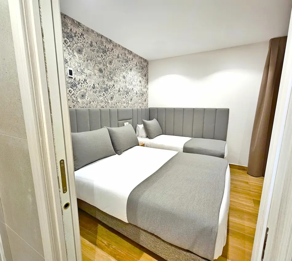 Habitación moderna con dos camas y decoración en tonos grises y papel tapiz floral.