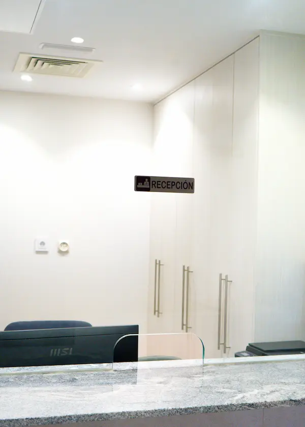 Mostrador de recepción con cartel en pared, mobiliario claro y luz de techo.