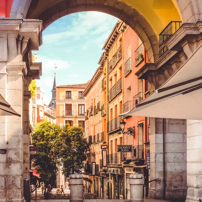 Calle con edificios coloridos y arcos de piedra, bajo un cielo azul con algunas nubes.