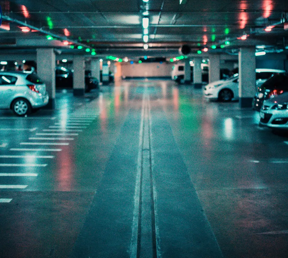 Estacionamiento subterráneo iluminado con luces de colores y varios automóviles estacionados.