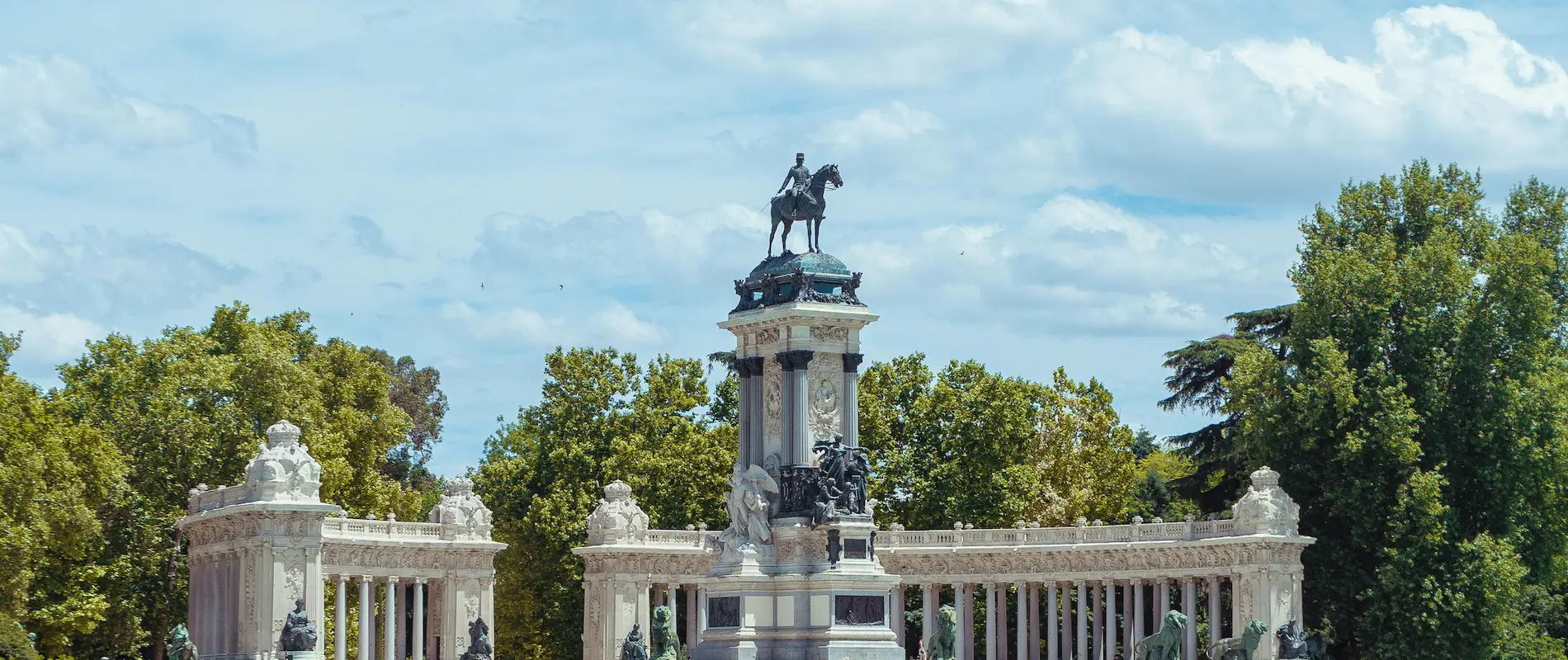 Monumento ecuestre sobre columnas clásicas, rodeado de vegetación y cielo parcialmente nublado.