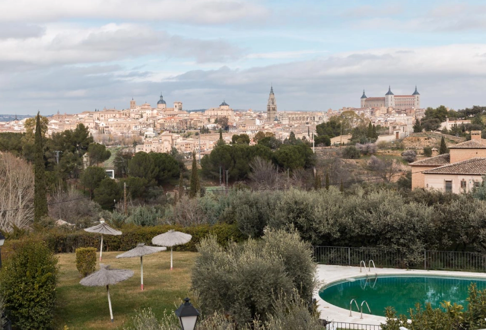Vista panorámica de una ciudad histórica con una piscina en primer plano y cielos nublados.