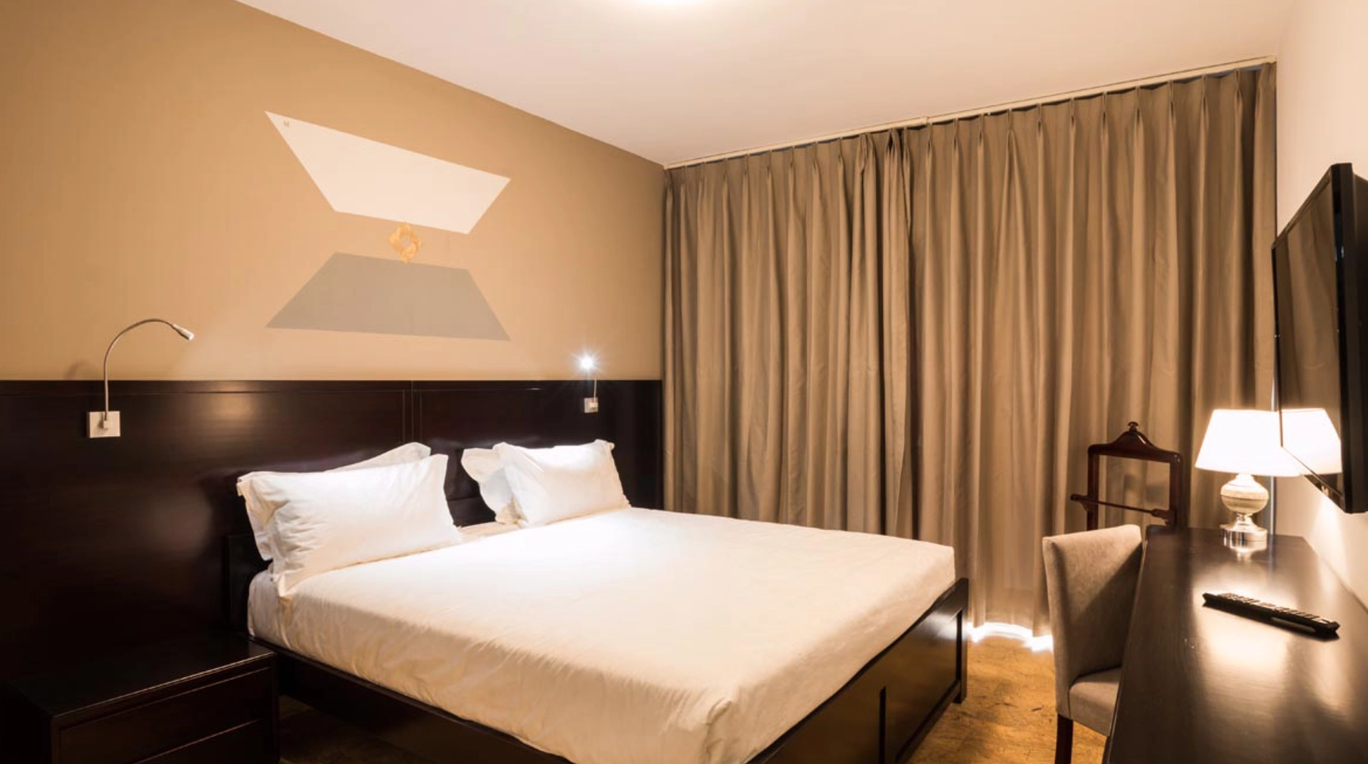 Habitación de hotel moderna con cama doble, escritorio y cortinas cerradas.