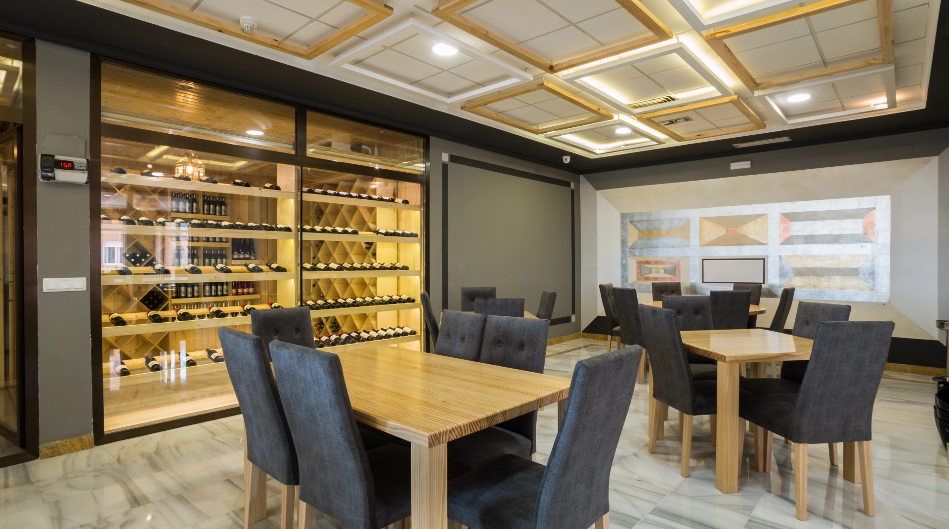 Restaurante moderno con sillas grises, mesas de madera y una bodega con botellas de vino.