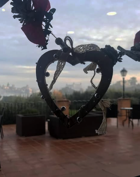 Corazón decorativo colgante con fondo de terraza y paisaje nublado.