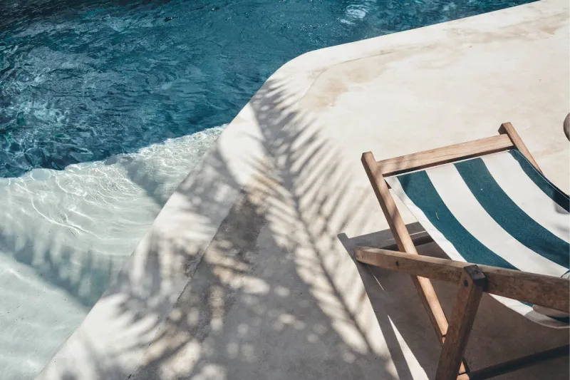 Transat à rayures sur une terrasse près d'une piscine ensoleillée.