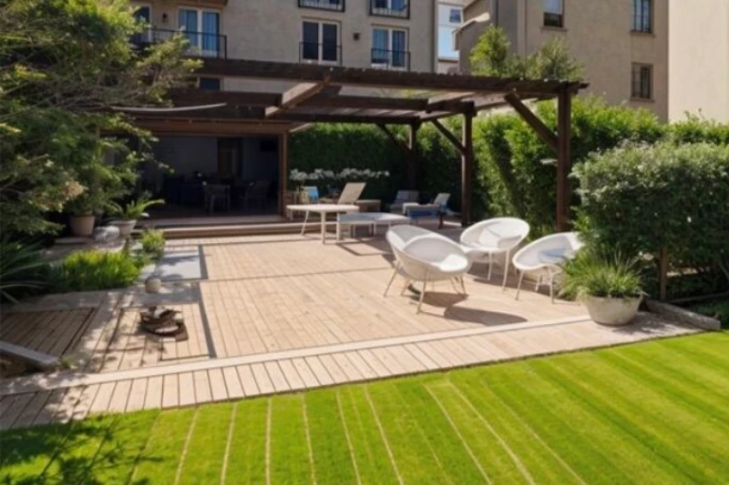 Terrasse en bois avec pergola et chaises blanches dans un jardin, bâtiment en arrière-plan.