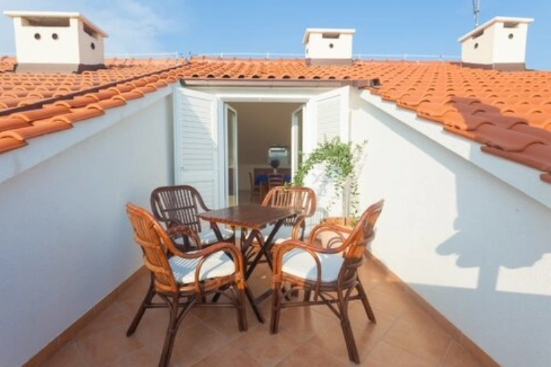 Salon de jardin en rotin sur une terrasse ensoleillée sous un toit en tuiles.