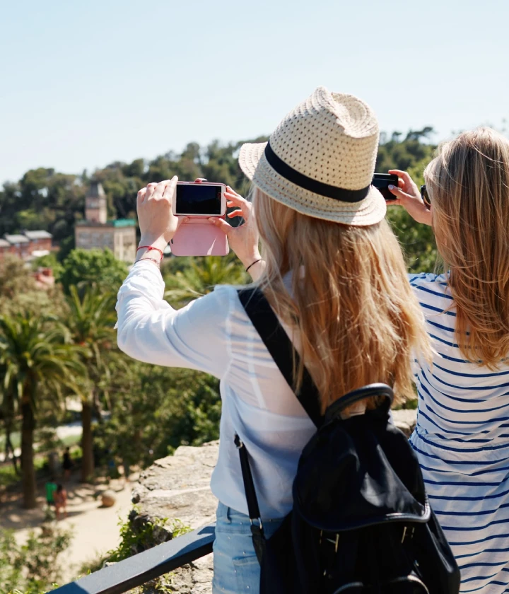 Dos personas toman fotos de un paisaje con sus teléfonos, rodeadas de árboles.