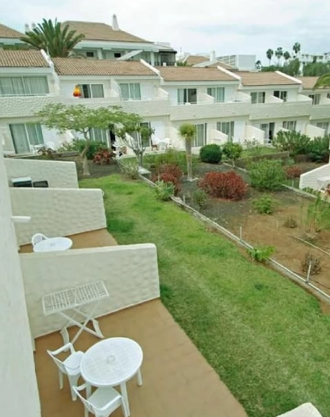 Terrazas de apartamentos con mesas y sillas blancas, rodeadas de jardines y plantas.