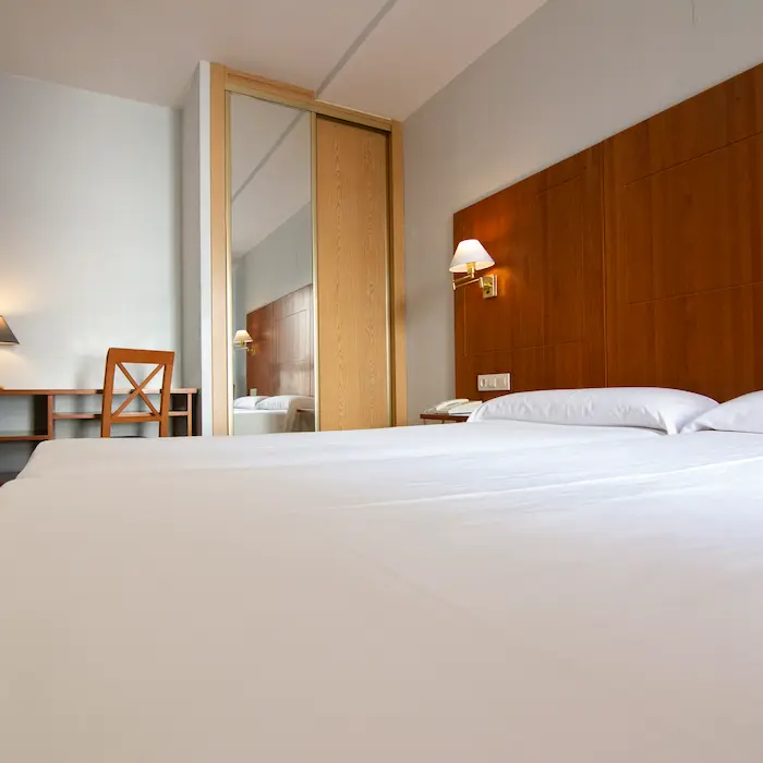 Habitación de hotel con cama doble, espejo, escritorio y lámpara de pared.