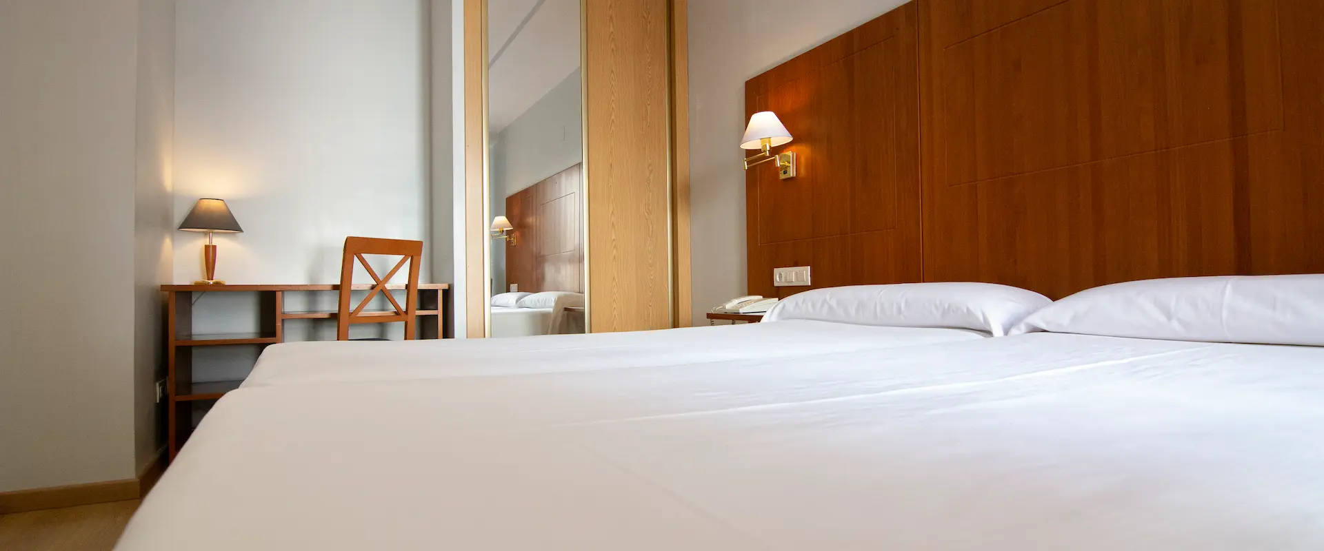Habitación de hotel con cama doble, escritorio, silla y lámparas en tonos cálidos.