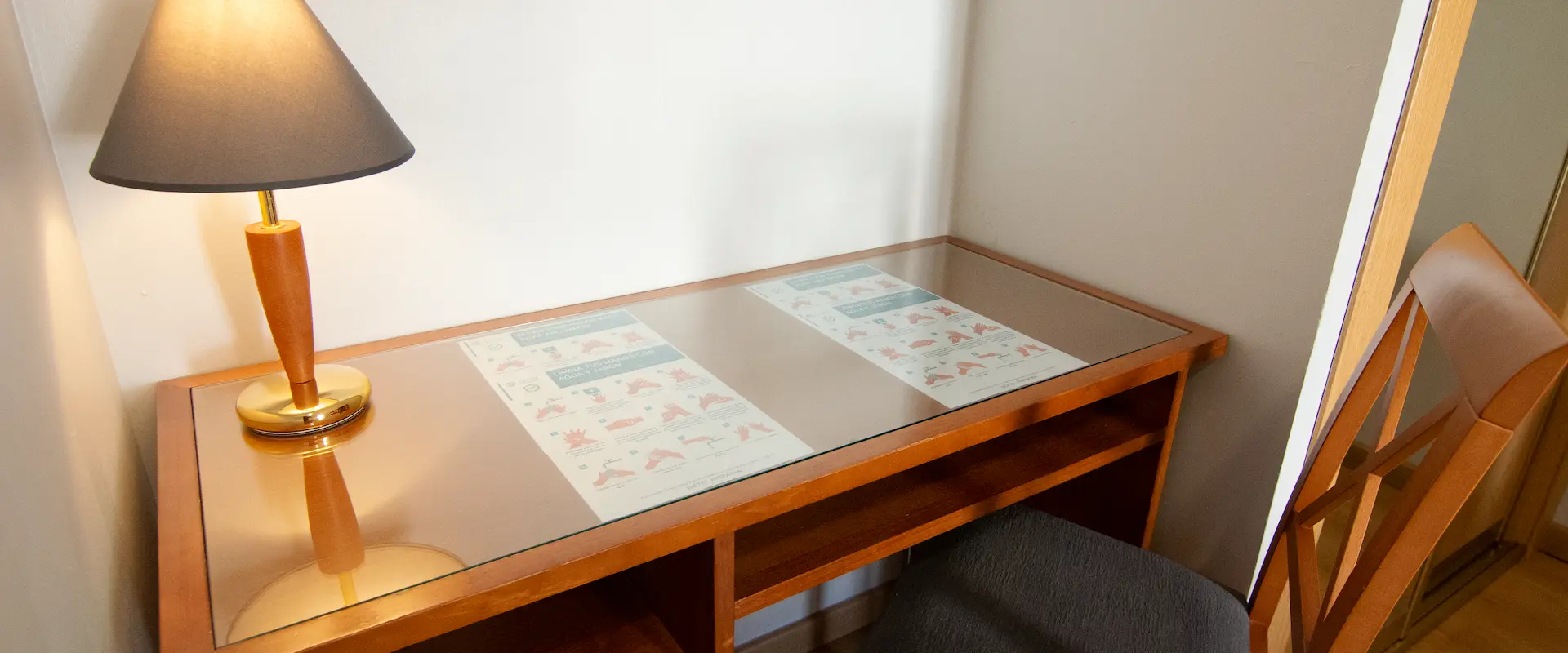 Mesa de madera con vidrio, lámpara encendida y folletos impresos debajo del cristal.