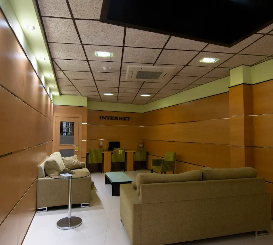 Sala de internet con sofás y computadoras en un ambiente con paredes de madera y techo de paneles.