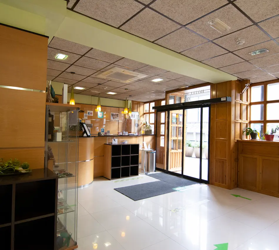 Recepción de hotel con mostrador de madera y puerta de vidrio automático junto a plantas.