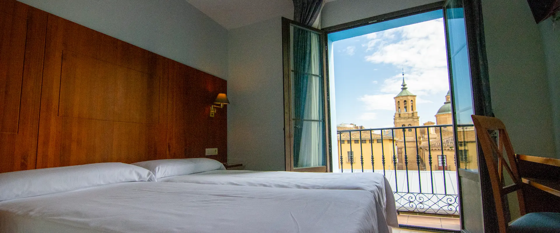 Habitación con dos camas y balcón con vista a una torre y cielo azul.
