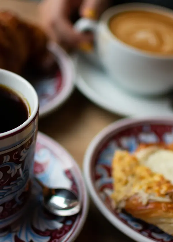 Tazas de café sobre platos decorados y un croissant en primer plano.
