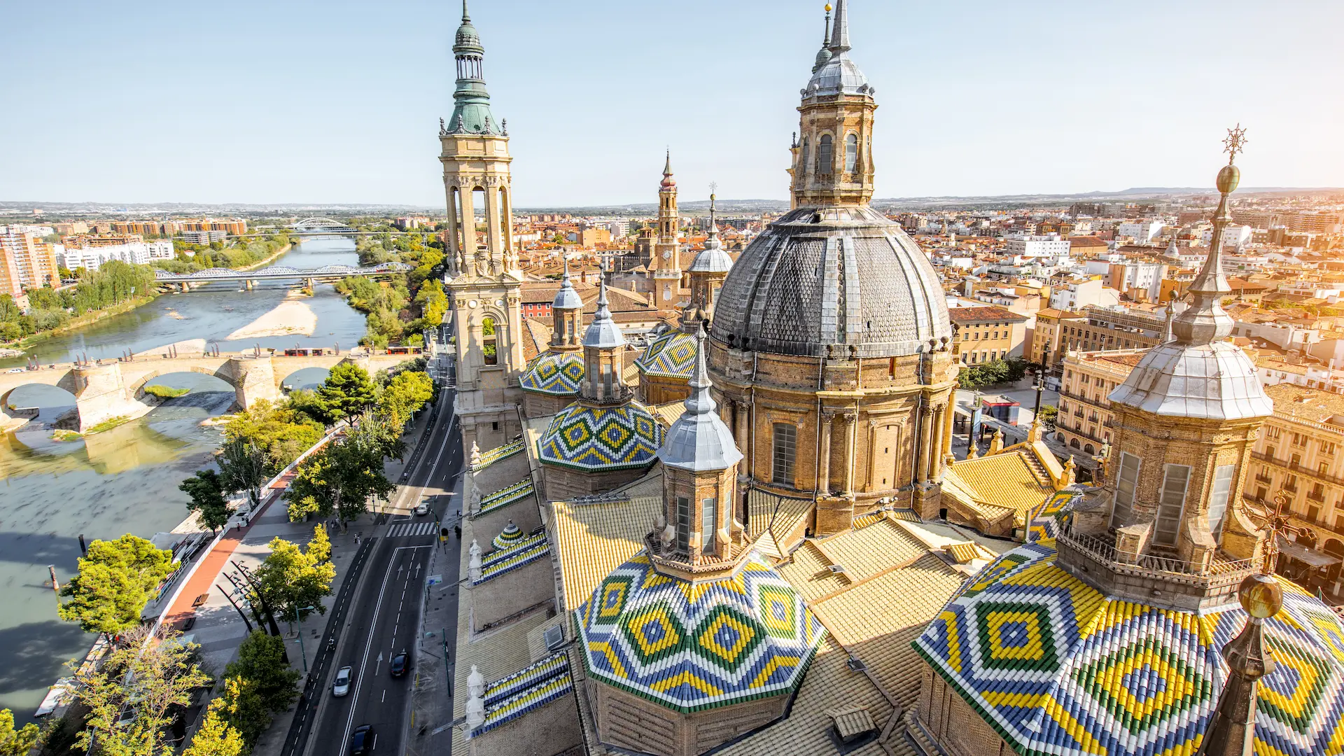 Catedral con cúpulas coloridas y río a un lado, vista de ciudad al fondo.