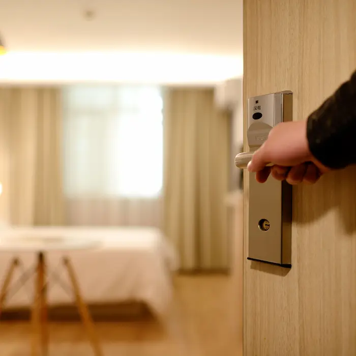 Mano abriendo la puerta de una habitación luminosa con cama y cortinas.