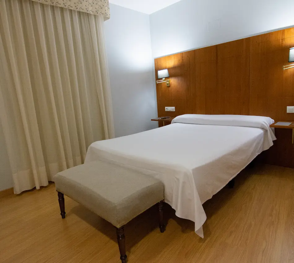 Habitación de hotel con cama, cortinas claras y lámparas en la pared de madera.