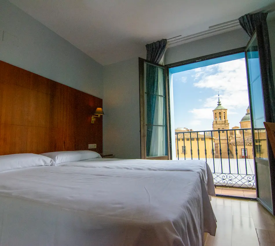 Habitación luminosa con camas gemelas y balcón con vista a un edificio histórico.
