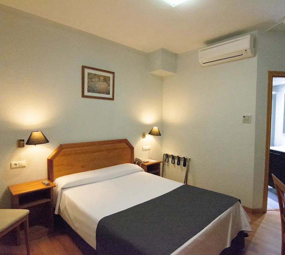 Habitación de hotel con cama doble, lámparas de pared, aire acondicionado y cuadro decorativo.