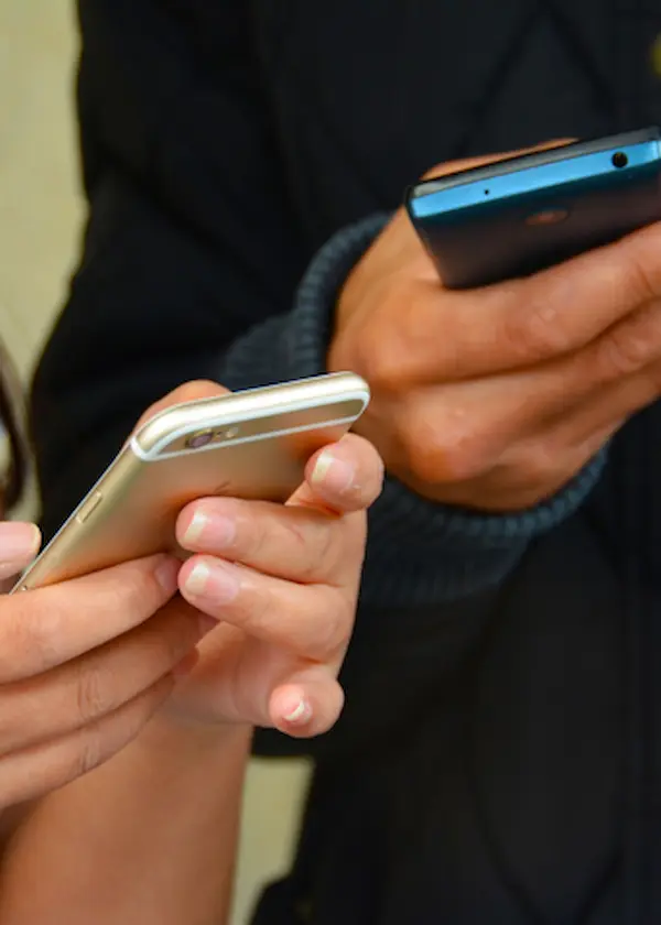 Dos personas usando teléfonos móviles, sosteniéndolos con ambas manos frente a un fondo oscuro.