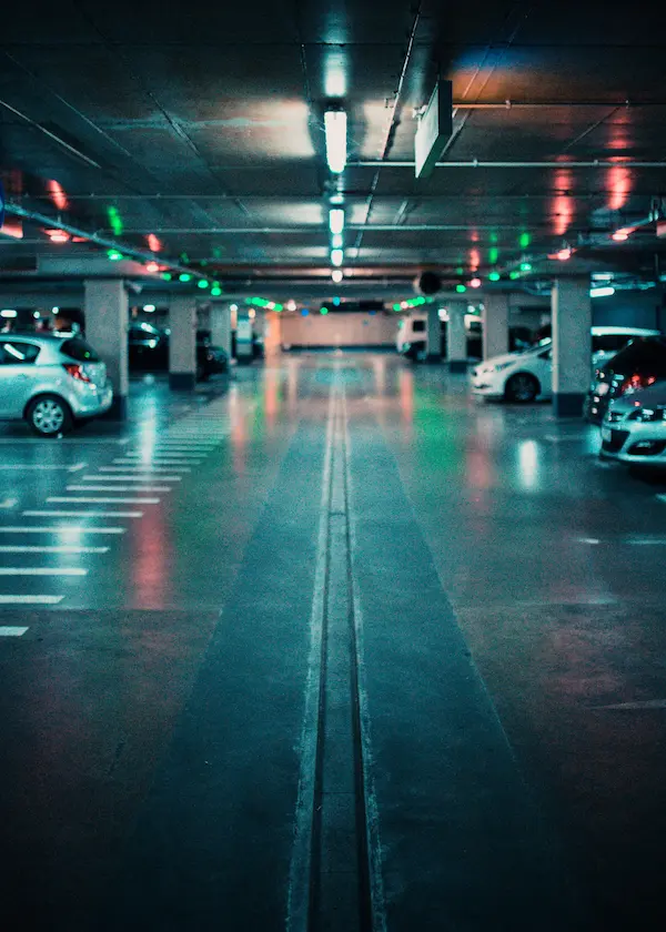 Estacionamiento subterráneo con luces coloridas y varios autos estacionados.